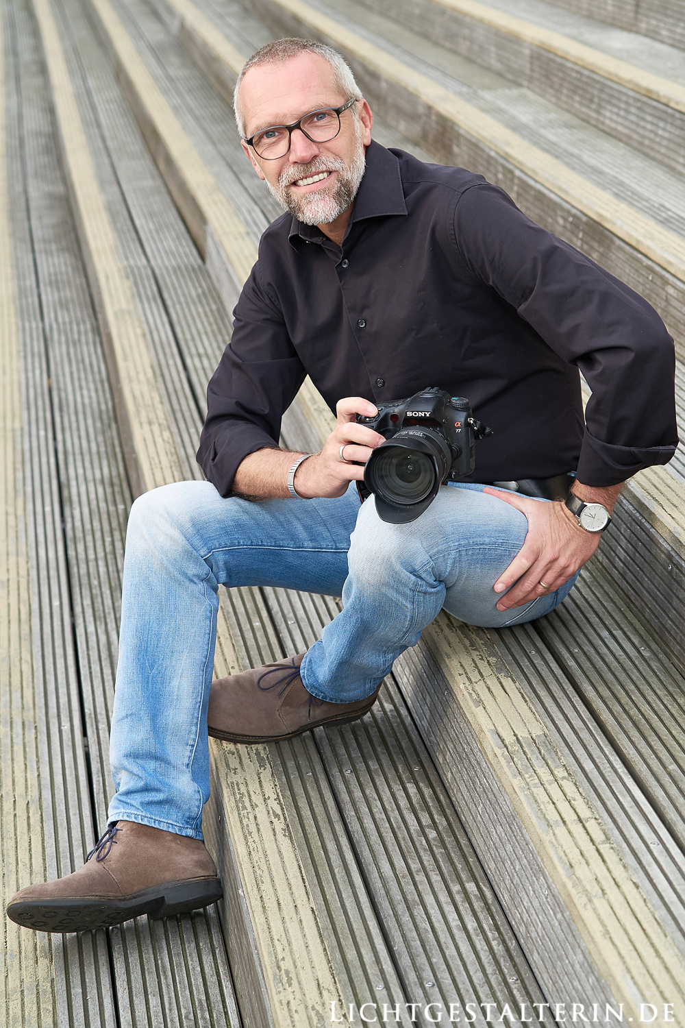 fotogener Mann mit Brille und Bart in Farbe, Ganzkörperporträt, mit Kamera, Sony, Uhr